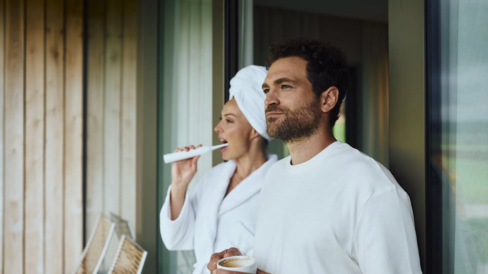 Paar sieht aus dem Fenster, während er Kaffee trinkt und sie ihre Zähne putzt